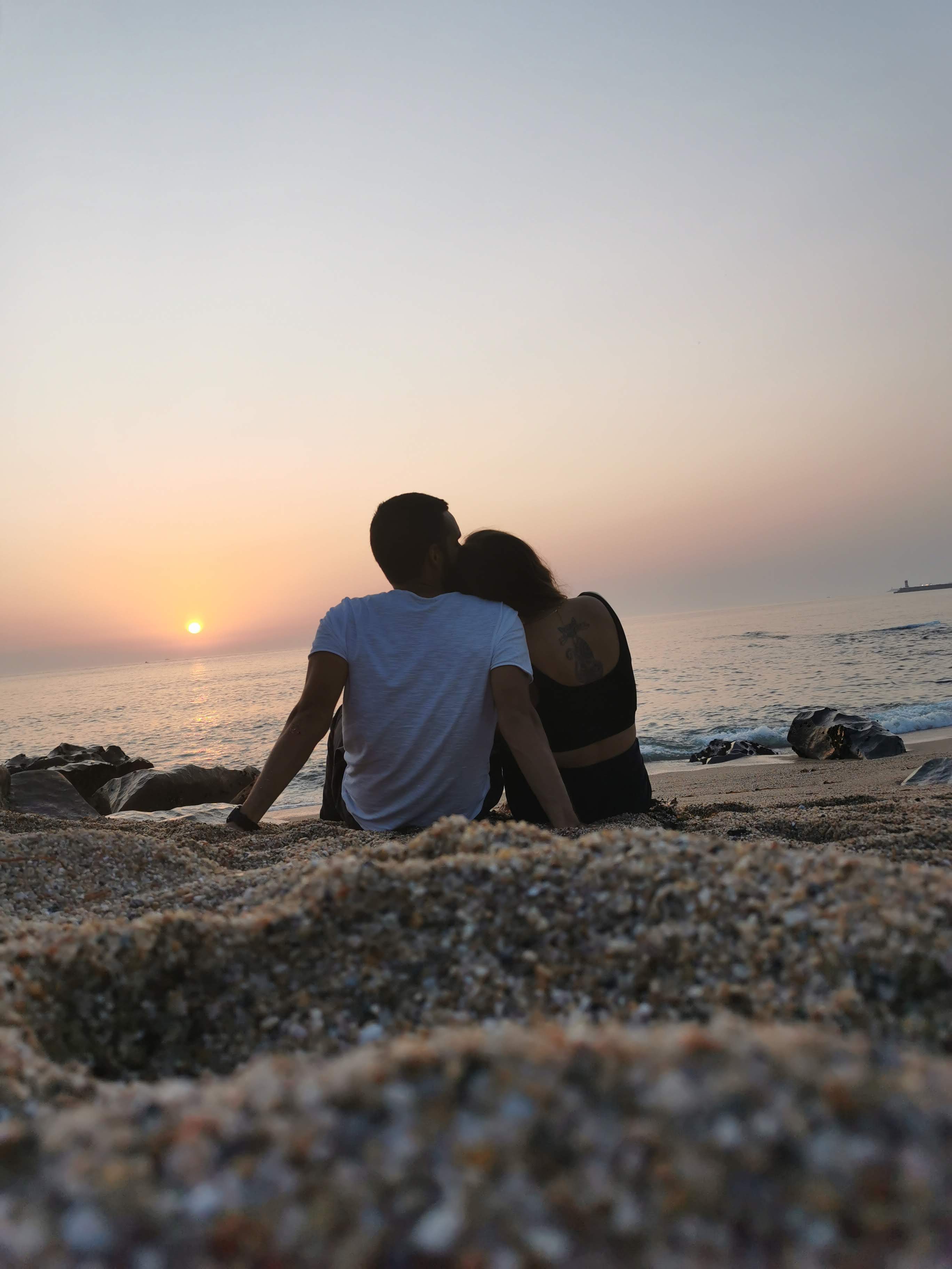 A couple sitting on the sand, watching the sunset over the ocean.